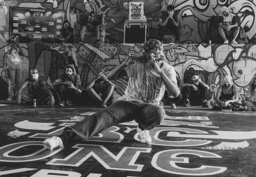 Il y a un homme qui danse entouré de treize personne qui le regarde.