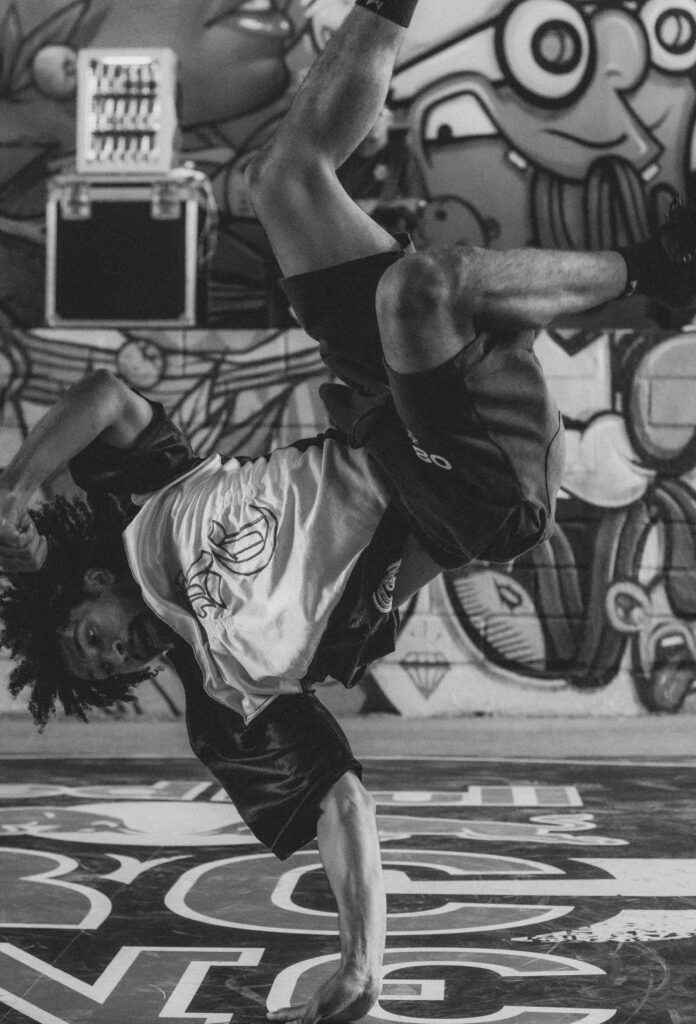 C'est un homme qui fait une pause artistique, il a les pieds dans les airs et il tiens sur une main, la tête à l'envers. Il est dehors, il a pleins de graffitis sur le mur et sol où qu'il est.